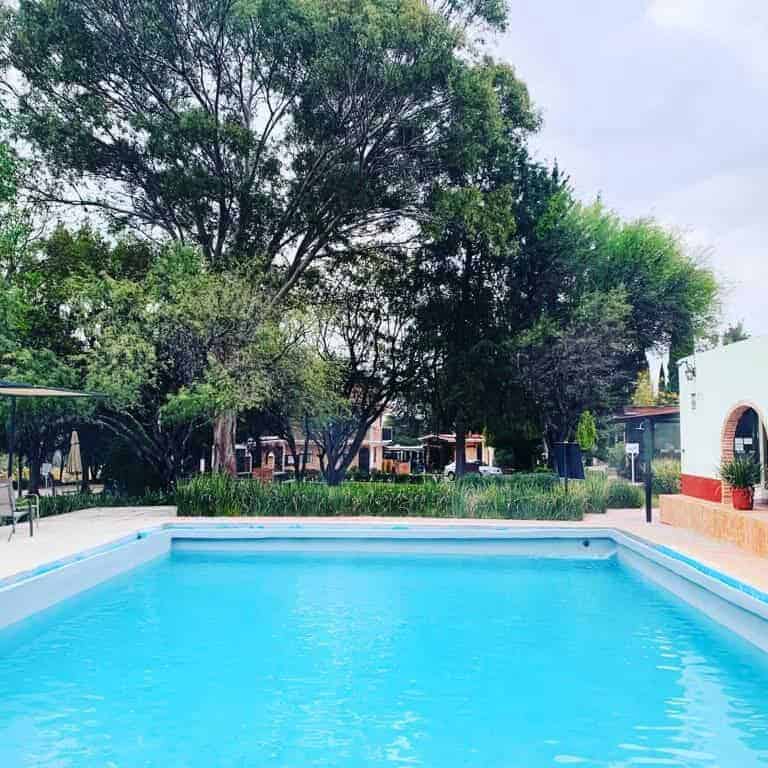 Piscina en Hotel San Ramon, rodeada de árboles y áreas verdes.