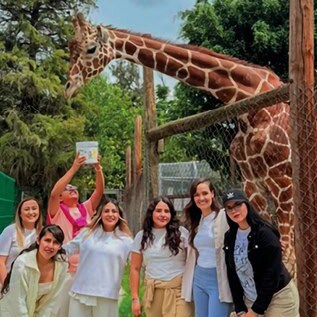 Grupo de personas en el Parque Zoológico de Irapuato con jirafa en fondo.