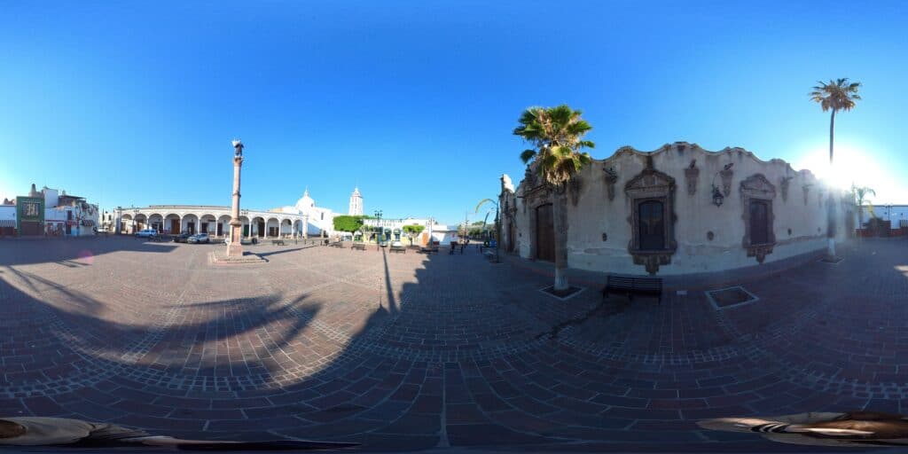 Vista 360° de la plaza principal de Apaseo el Grande, Guanajuato, con portales, una columna monumental y una fachada de cantera labrada.