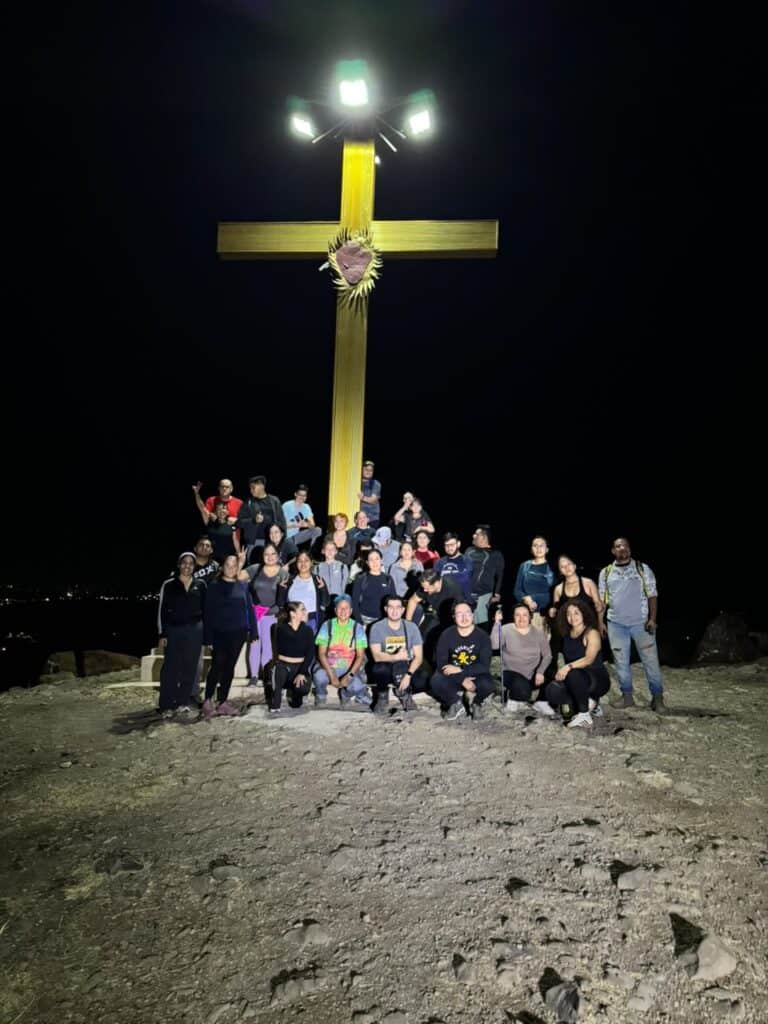 Grupo de personas en campamento con cruz iluminada en fondo nocturno.