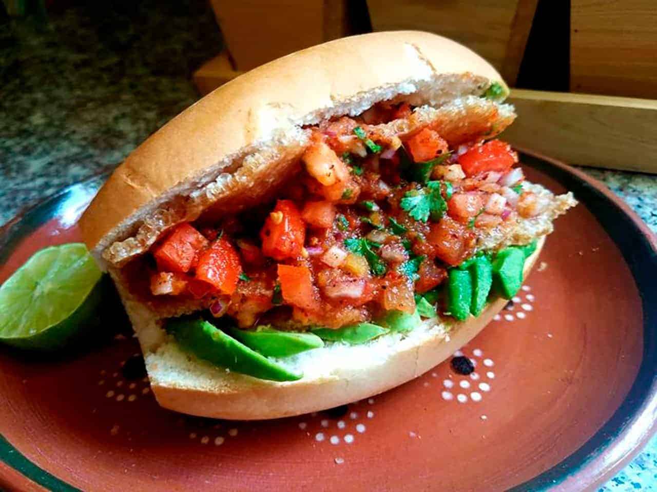 Mexican sandwich with meat, guacamole, and fresh vegetables.