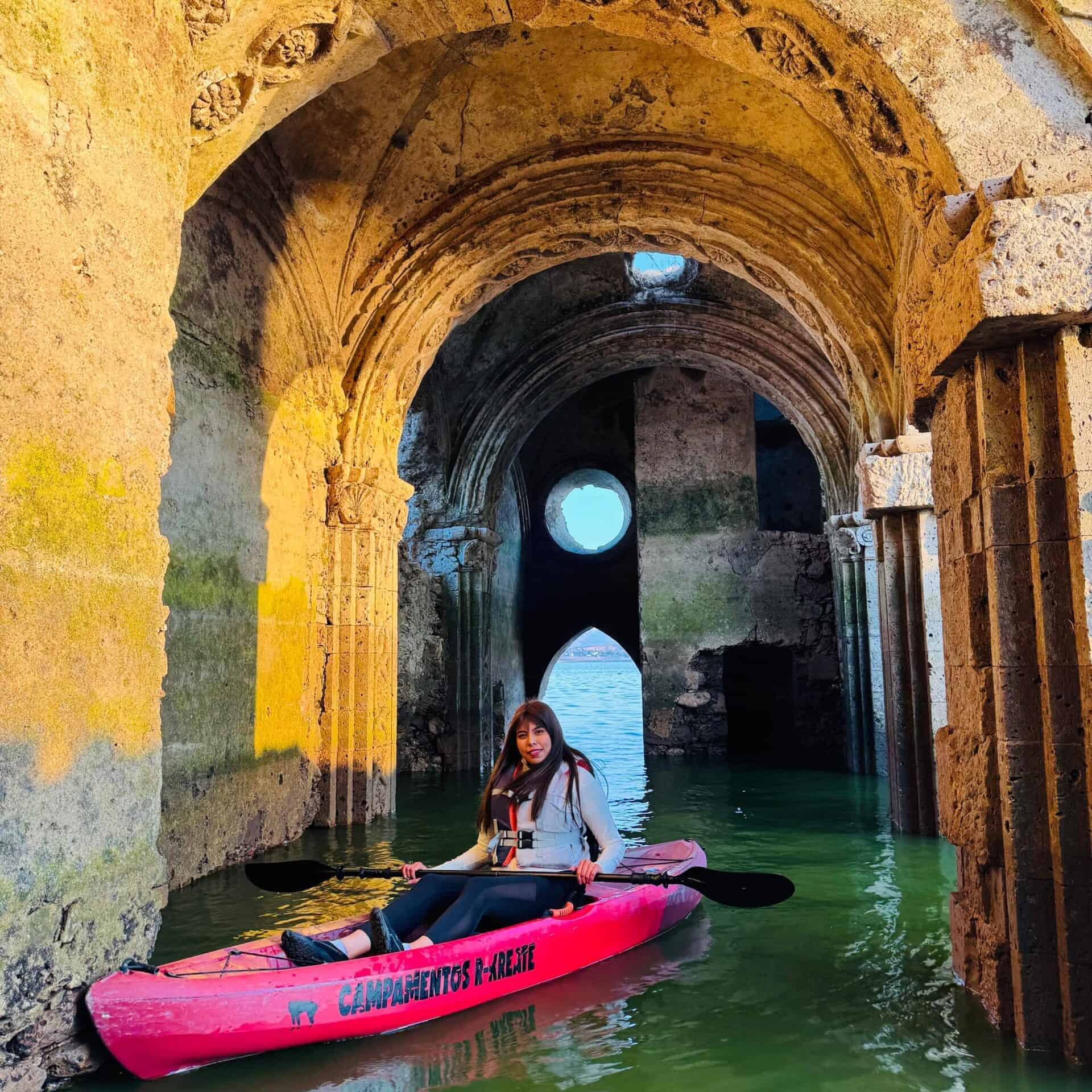 Persona haciendo kayak en un sitio histórico con arcos y agua.
