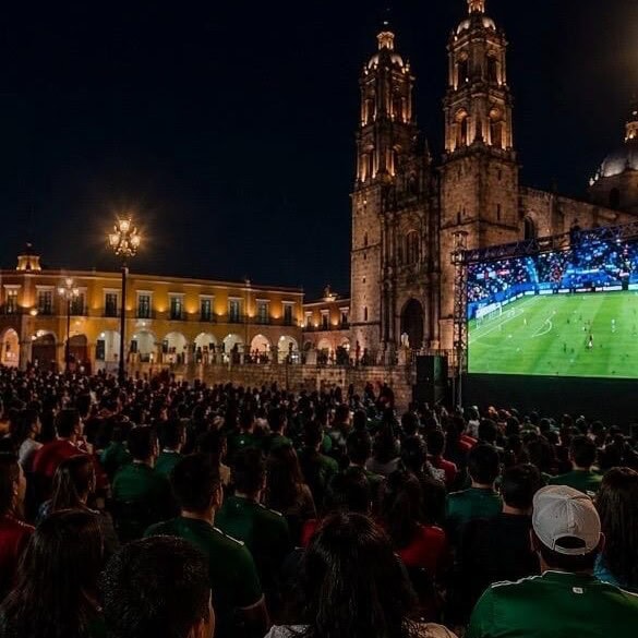 Torre de iglesia histórica en Guanajuato durante noche, con espectadores viendo un partido de fútbol.