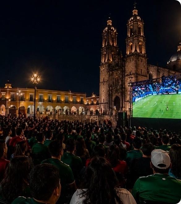 Torre de iglesia histórica en Guanajuato durante noche, con espectadores viendo un partido de fútbol.