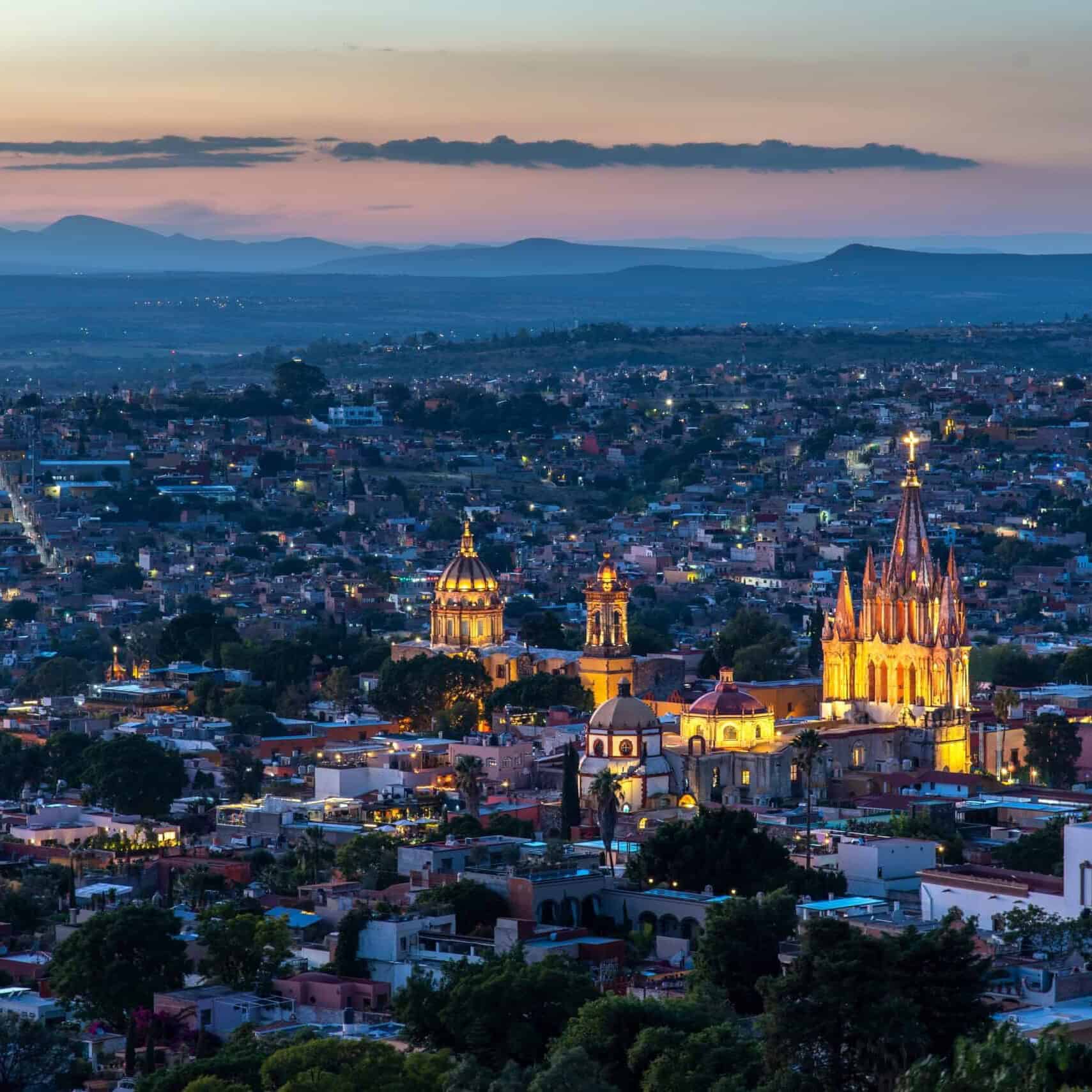 Vista nocturna de Guanajuato con catedrales iluminadas y paisaje montañoso.