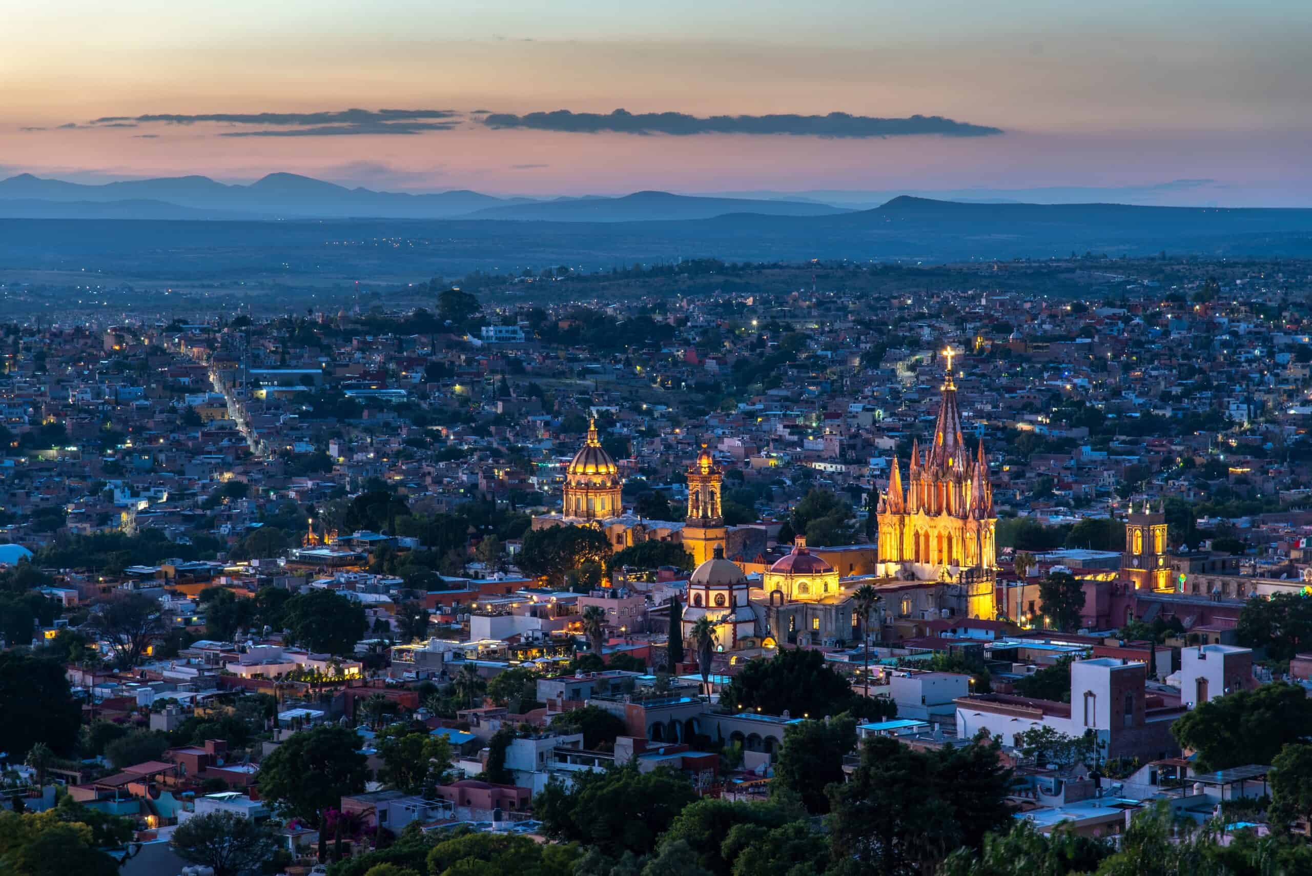 Vista nocturna de Guanajuato con catedrales iluminadas y paisaje montañoso.