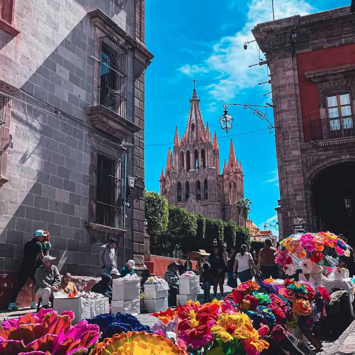 Vista de San Miguel de Allende con iglesia y mercado de flores coloridas.