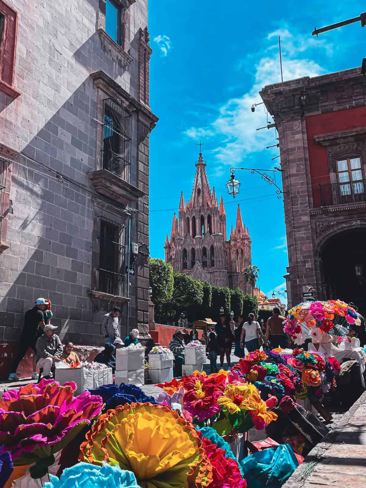 Vista de San Miguel de Allende con iglesia y mercado de flores coloridas.