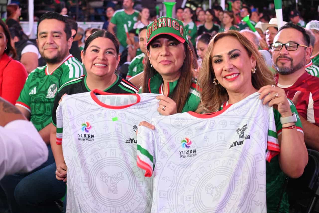 Aficionados mexicanos en un evento deportivo con camisetas y banderas de Yuriria y México.
