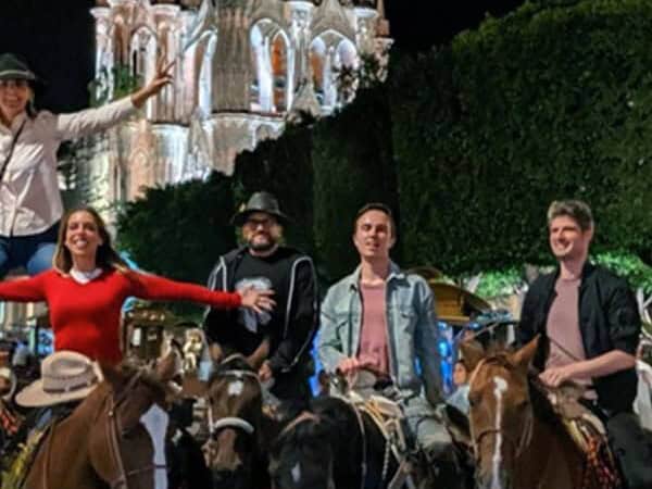 Grupo de turistas a caballo de noche frente a la Parroquia de San Miguel Arcángel iluminada, en San Miguel de Allende.