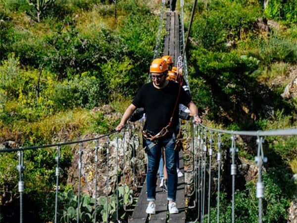 Persona cruzando un puente colgante entre vegetación en San Miguel Parque de Aventura.