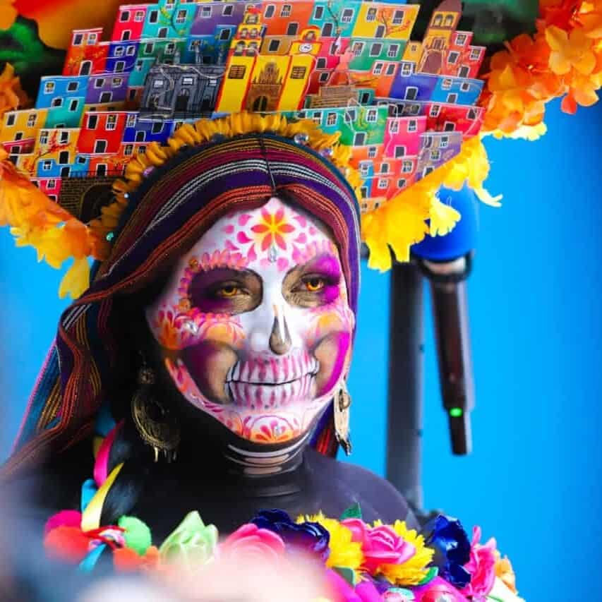 Mujer con maquillaje de calavera y vestuario colorido en Guanajuato durante festividad.