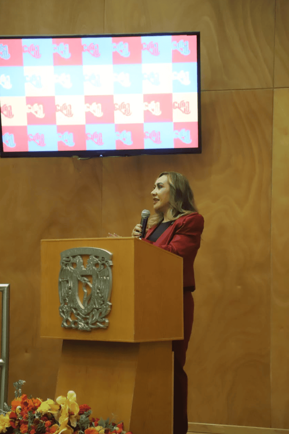 Mujer hablando en evento de turismo en Guanajuato con logo de UNAM en pantalla.