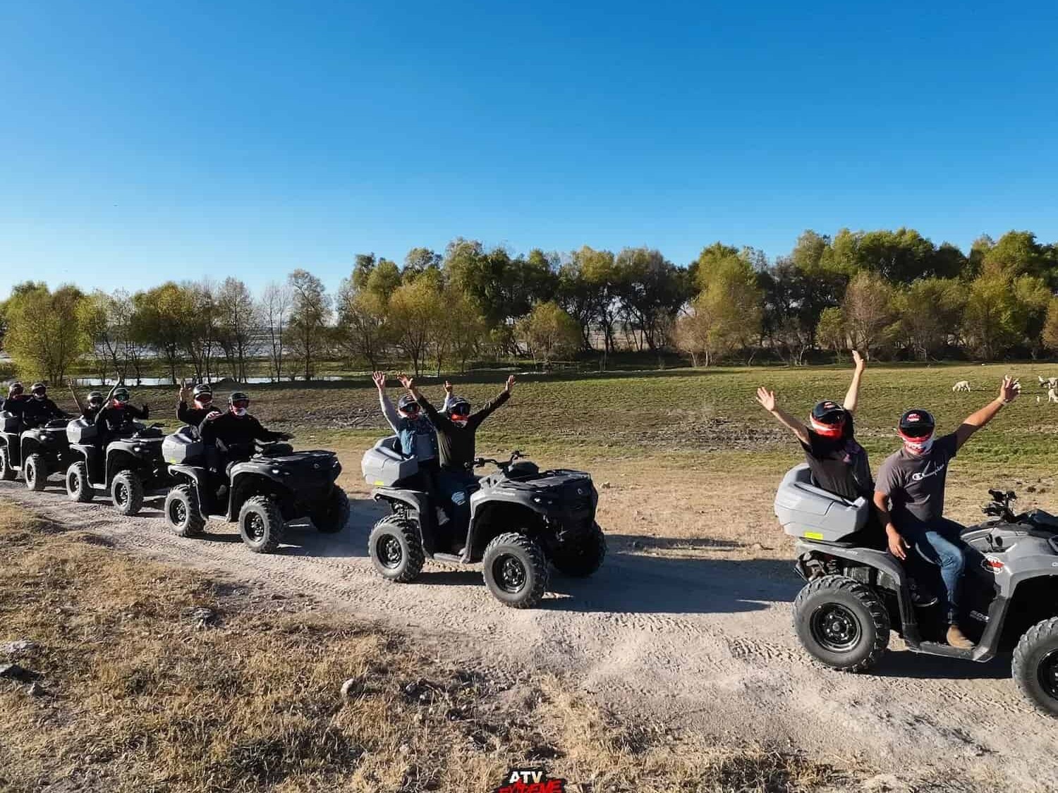 Group of travelers waving from their ATVs on a path next to the dam.