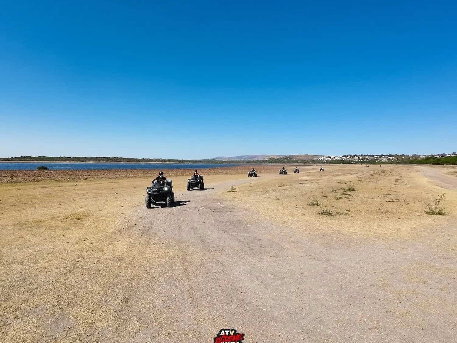 ATVs riding along a dirt road by the edge of the dam.