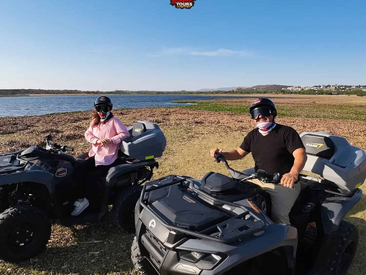 Couple on ATVs at the edge of the dam, with the water in the background.