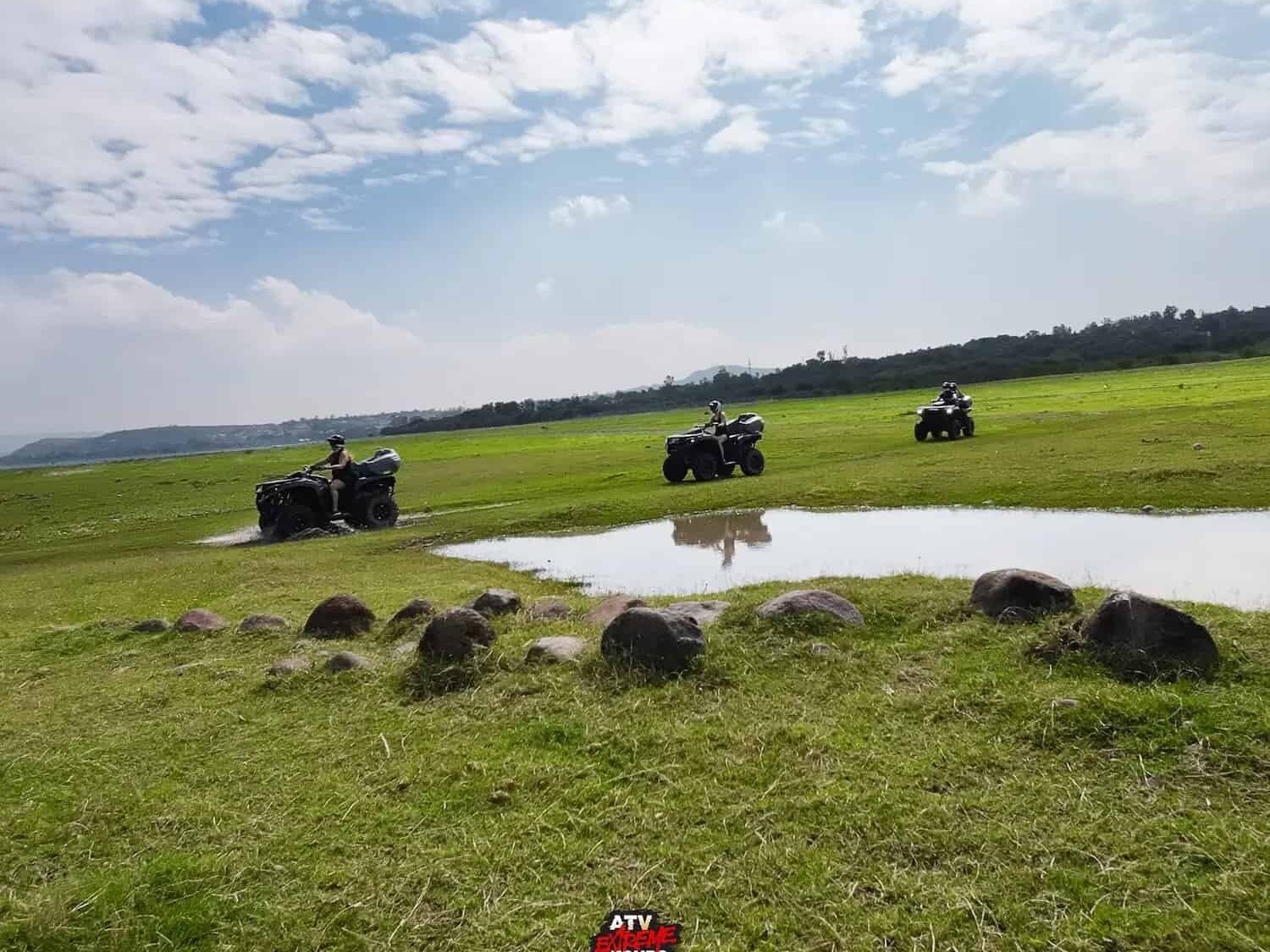 ATVs in a green field with a pond, during the rainy season.