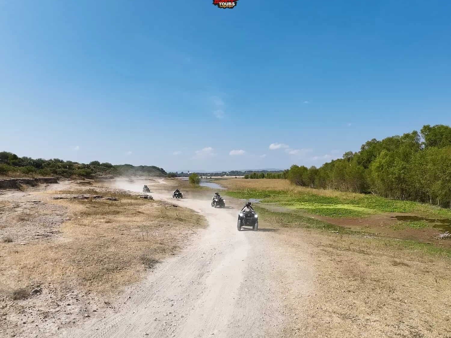 ATVs kicking up dust on a dirt road through the countryside.