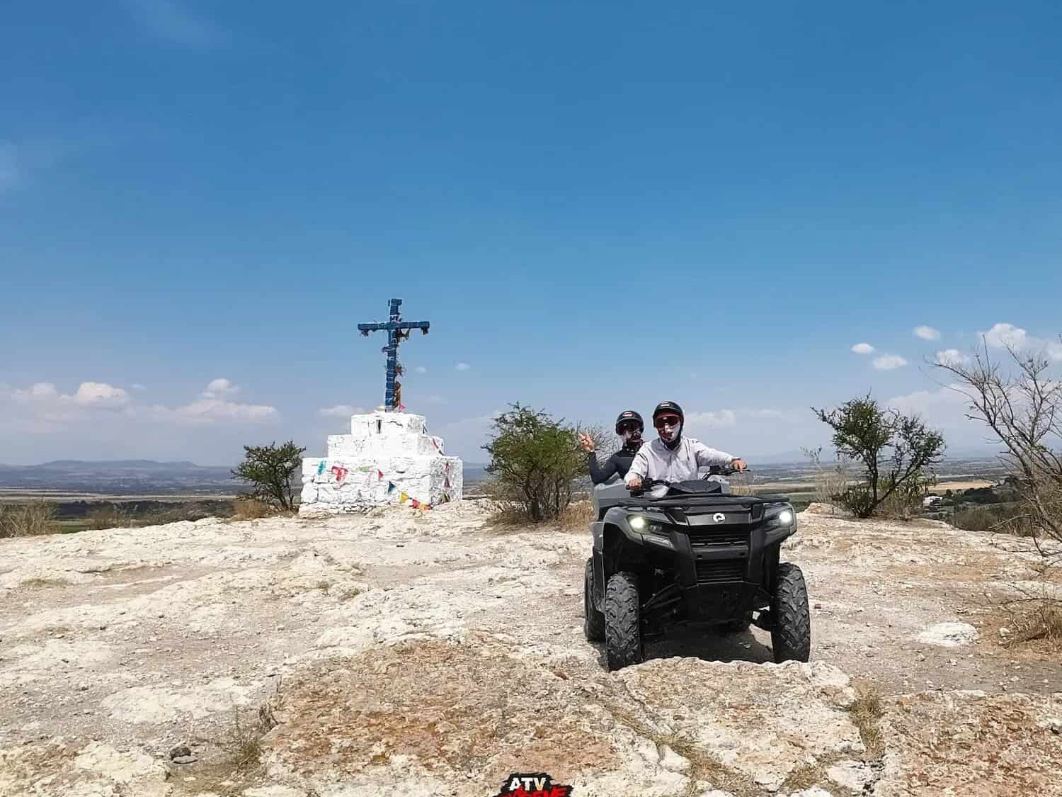 Couple on an ATV at a natural viewpoint with a white cross, in the surroundings of San Miguel de Allende.