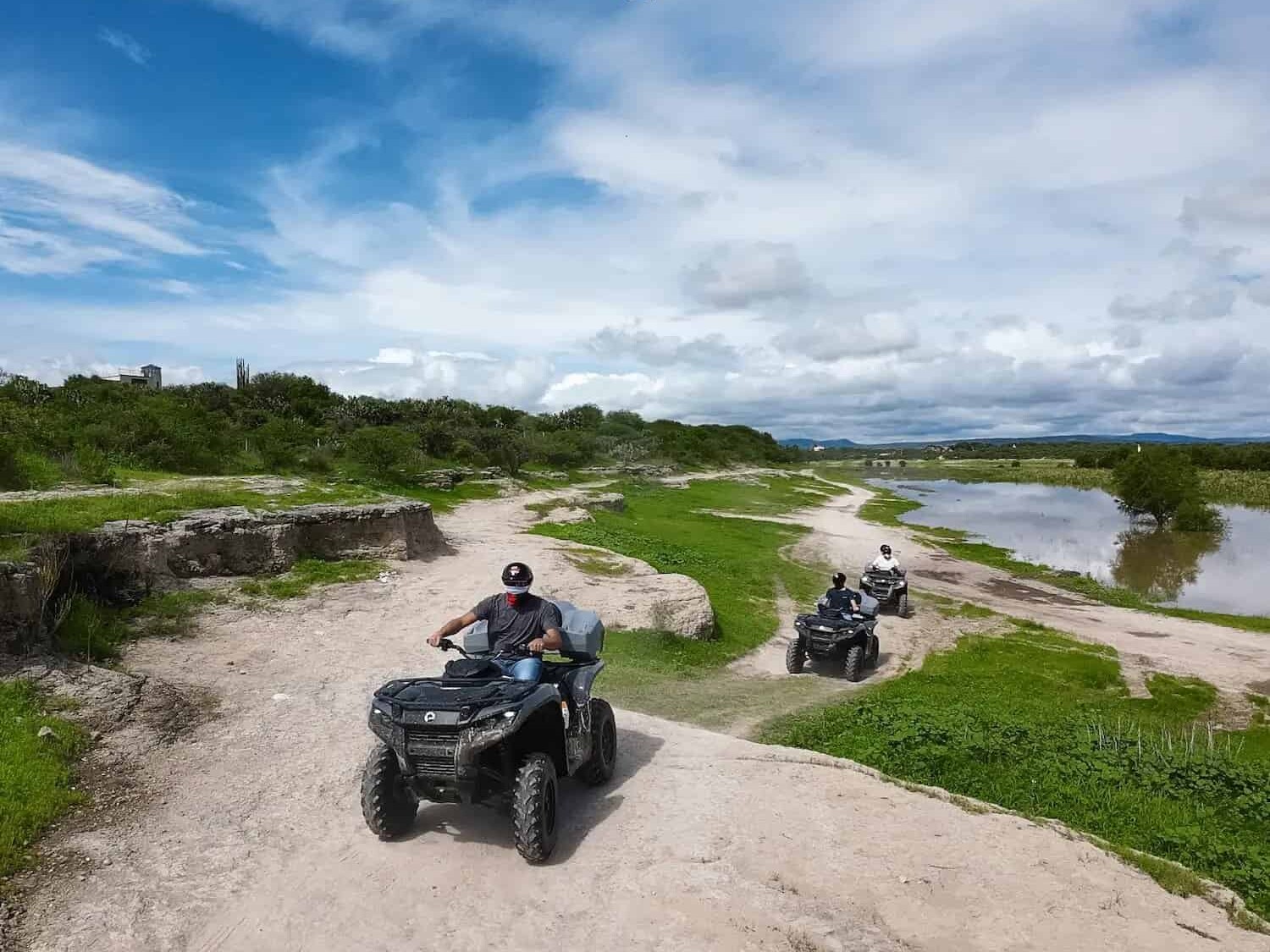 ATVs on a dirt road next to a river, surrounded by vegetation.