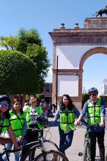 Bicycling group with helmets and vests in front of the Arco de la Calzada in León, Guanajuato.