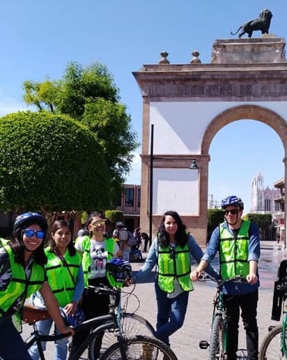 Grupo en bicicleta con casco y chaleco frente al Arco de la Calzada de León, Guanajuato.