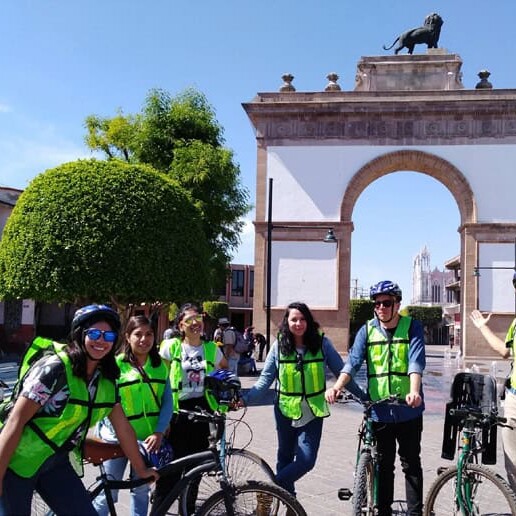 Bicycling group with helmets and vests in front of the Arco de la Calzada in León, Guanajuato.