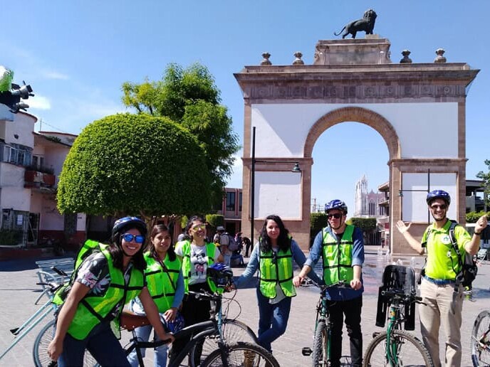 Grupo en bicicleta con casco y chaleco frente al Arco de la Calzada de León, Guanajuato.