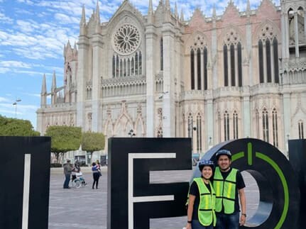 Couple wearing helmets in front of the León letters and the Templo Expiatorio, Guanajuato.