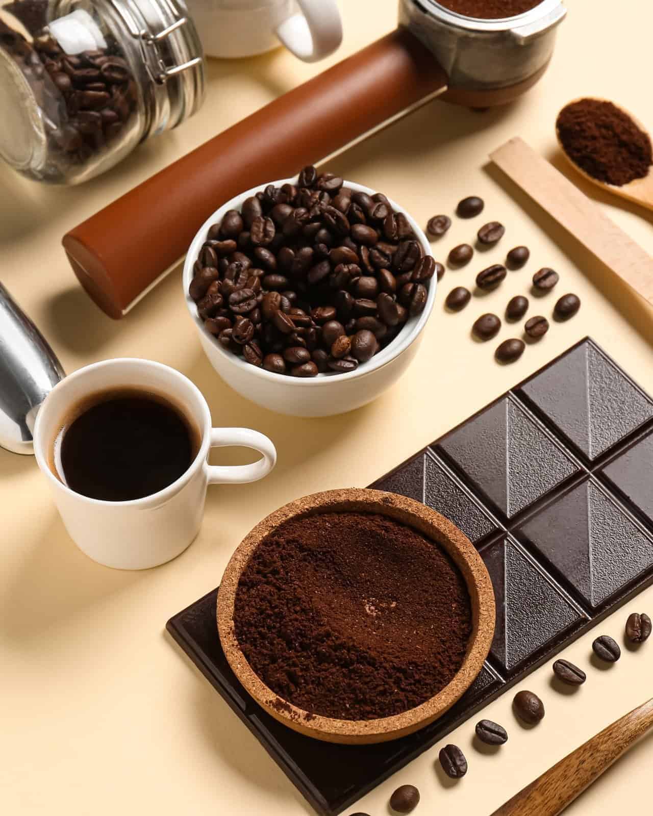 Taza de café con granos, café molido y una tableta de chocolate amargo.