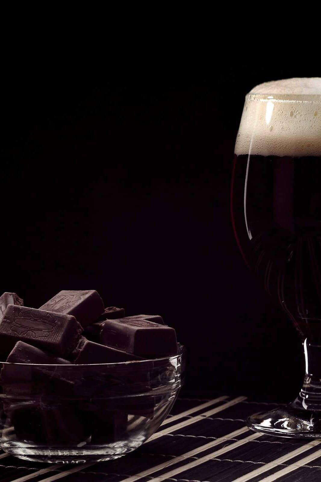 Copa de cerveza oscura junto a un tazón con trozos de chocolate amargo.