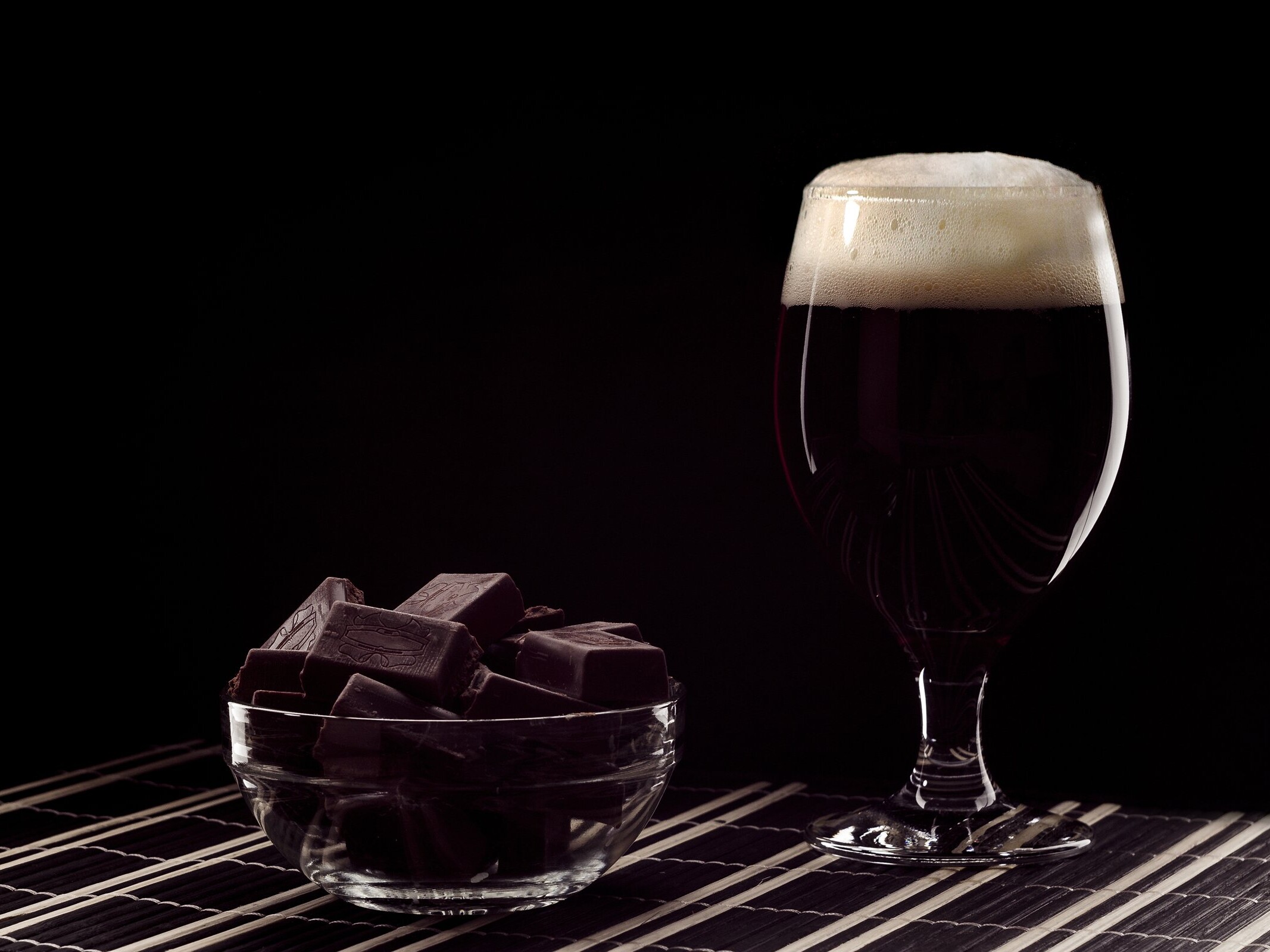 Copa de cerveza oscura junto a un tazón con trozos de chocolate amargo.