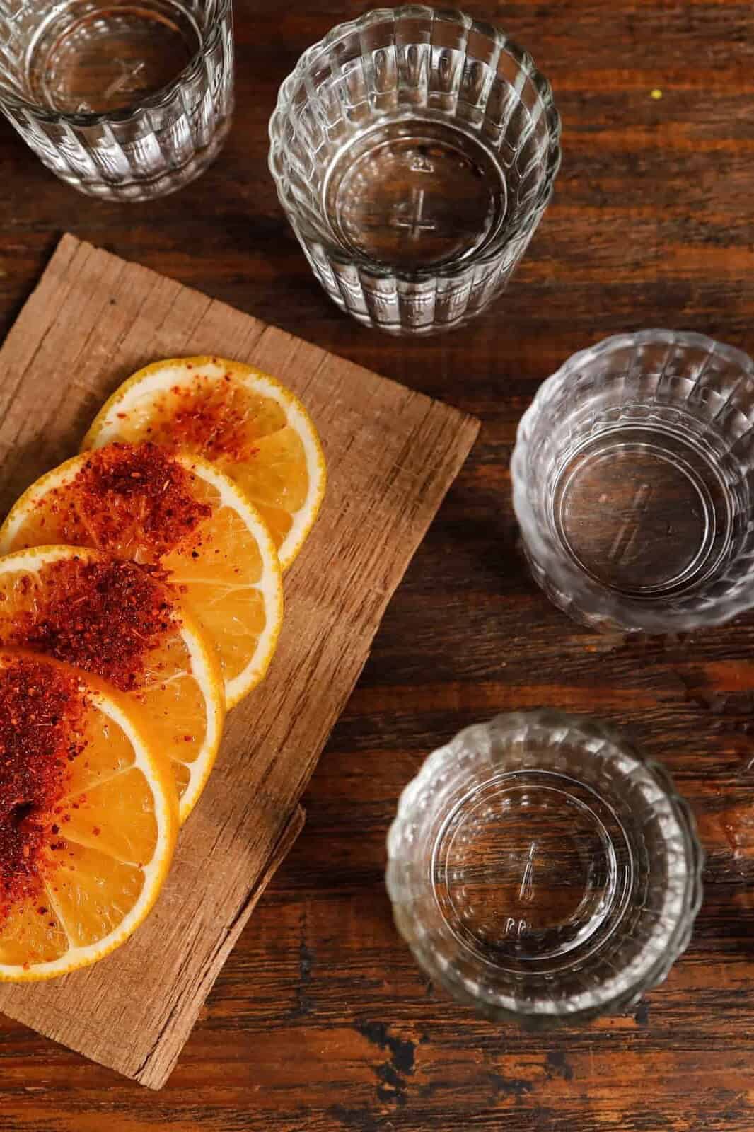 Vasos de mezcal con rodajas de naranja sobre una tabla de madera.