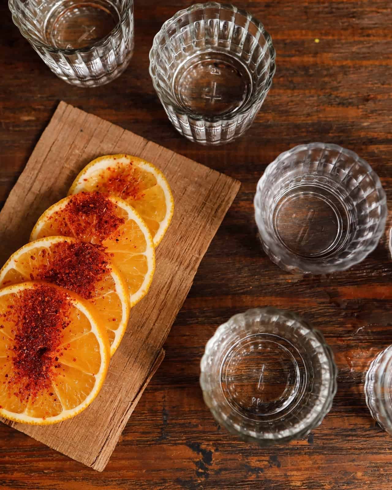 Vasos de mezcal con rodajas de naranja sobre una tabla de madera.