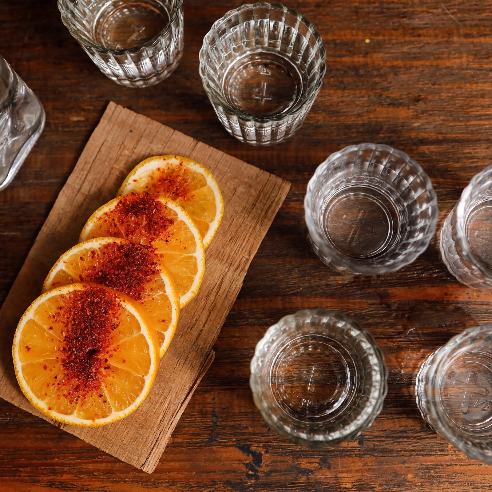 Vasos de mezcal con rodajas de naranja sobre una tabla de madera.