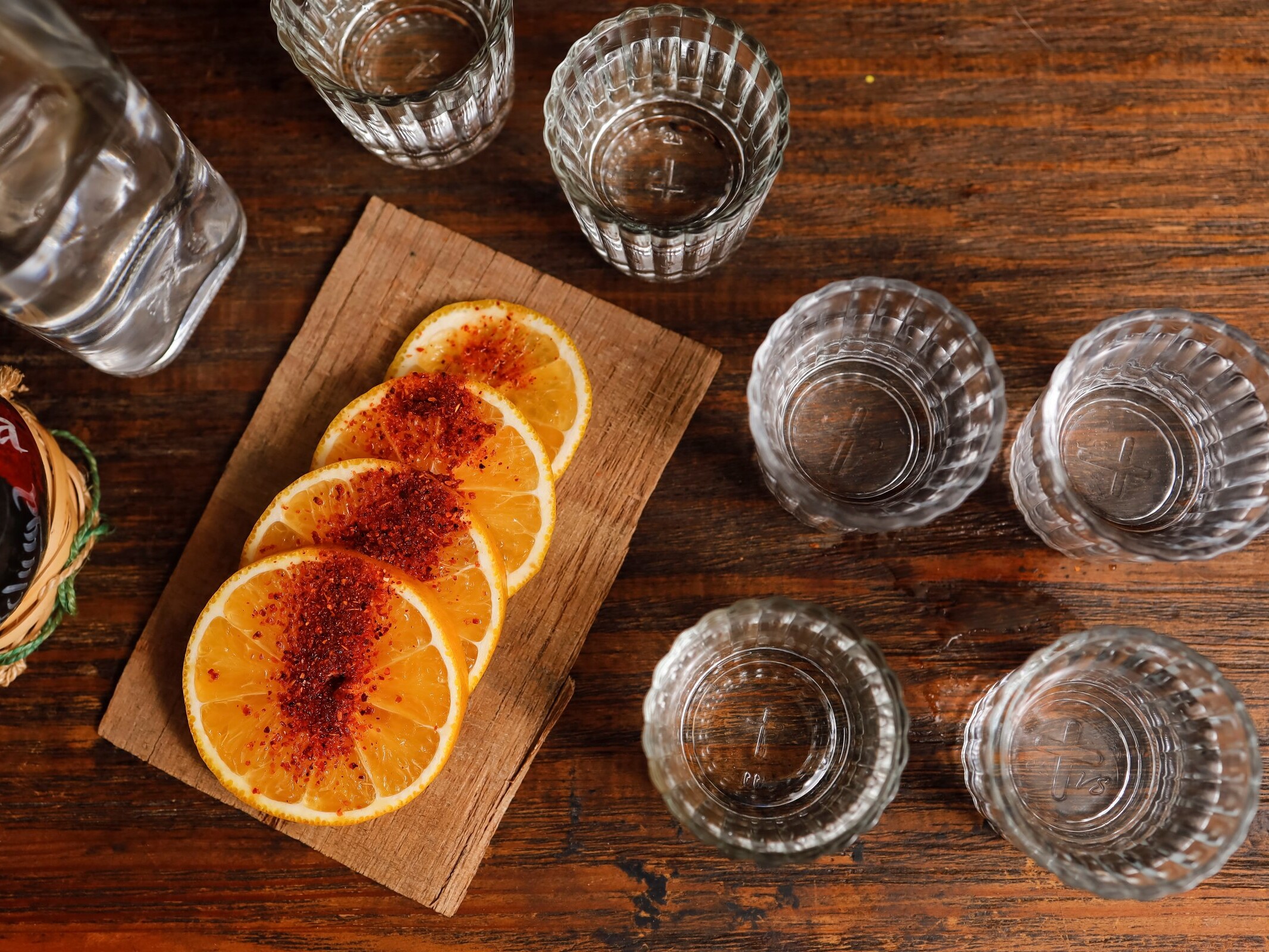 Vasos de mezcal con rodajas de naranja sobre una tabla de madera.