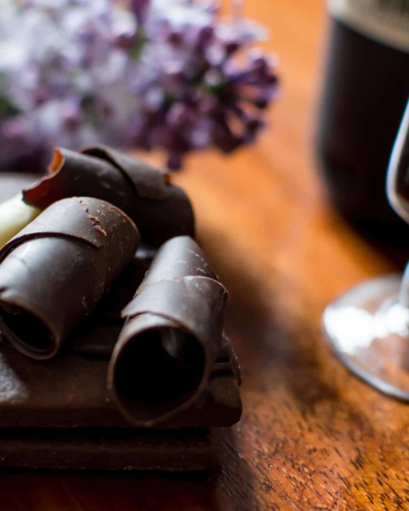 Copa de vino tinto junto a un postre de chocolate con rizos de chocolate amargo y blanco.