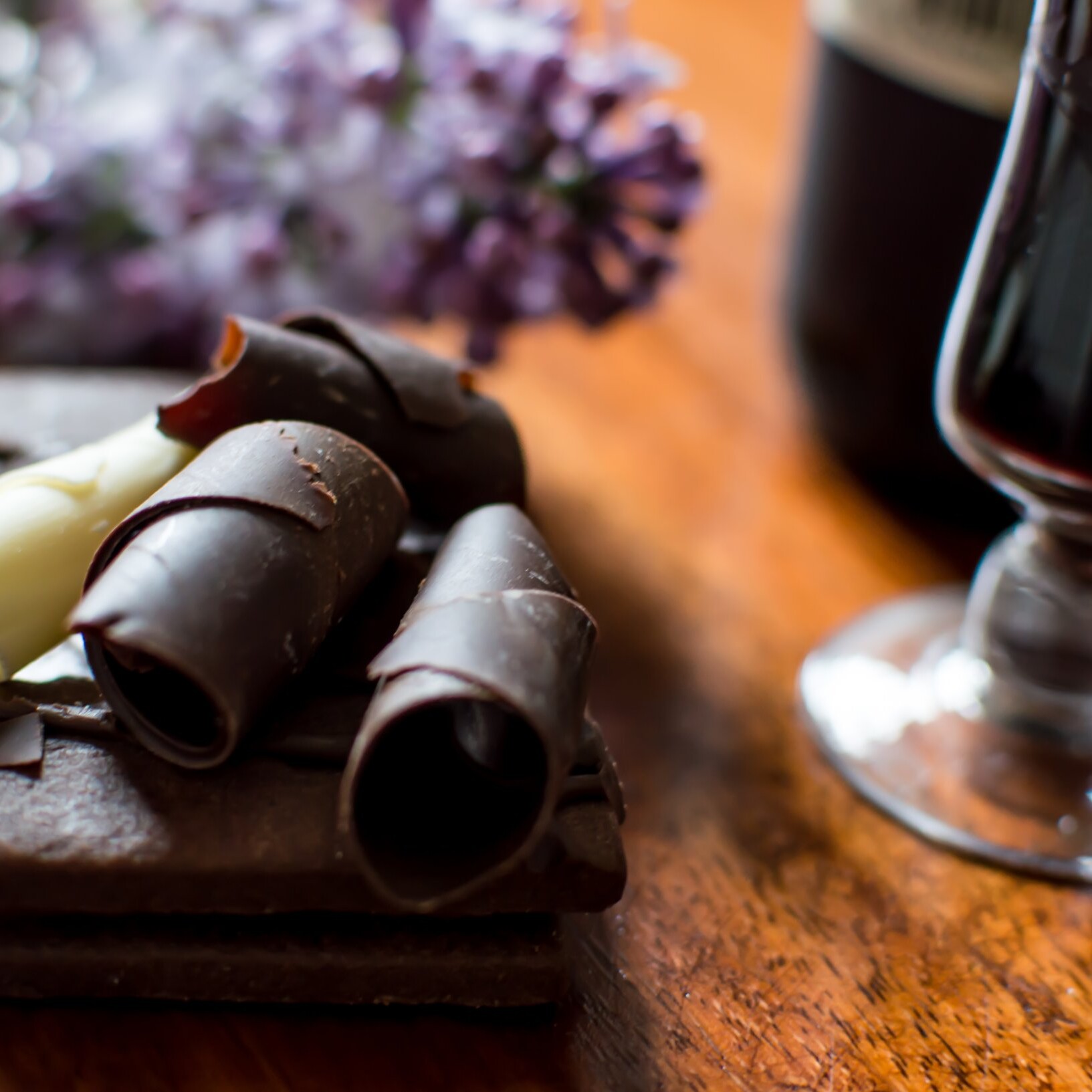 Copa de vino tinto junto a un postre de chocolate con rizos de chocolate amargo y blanco.