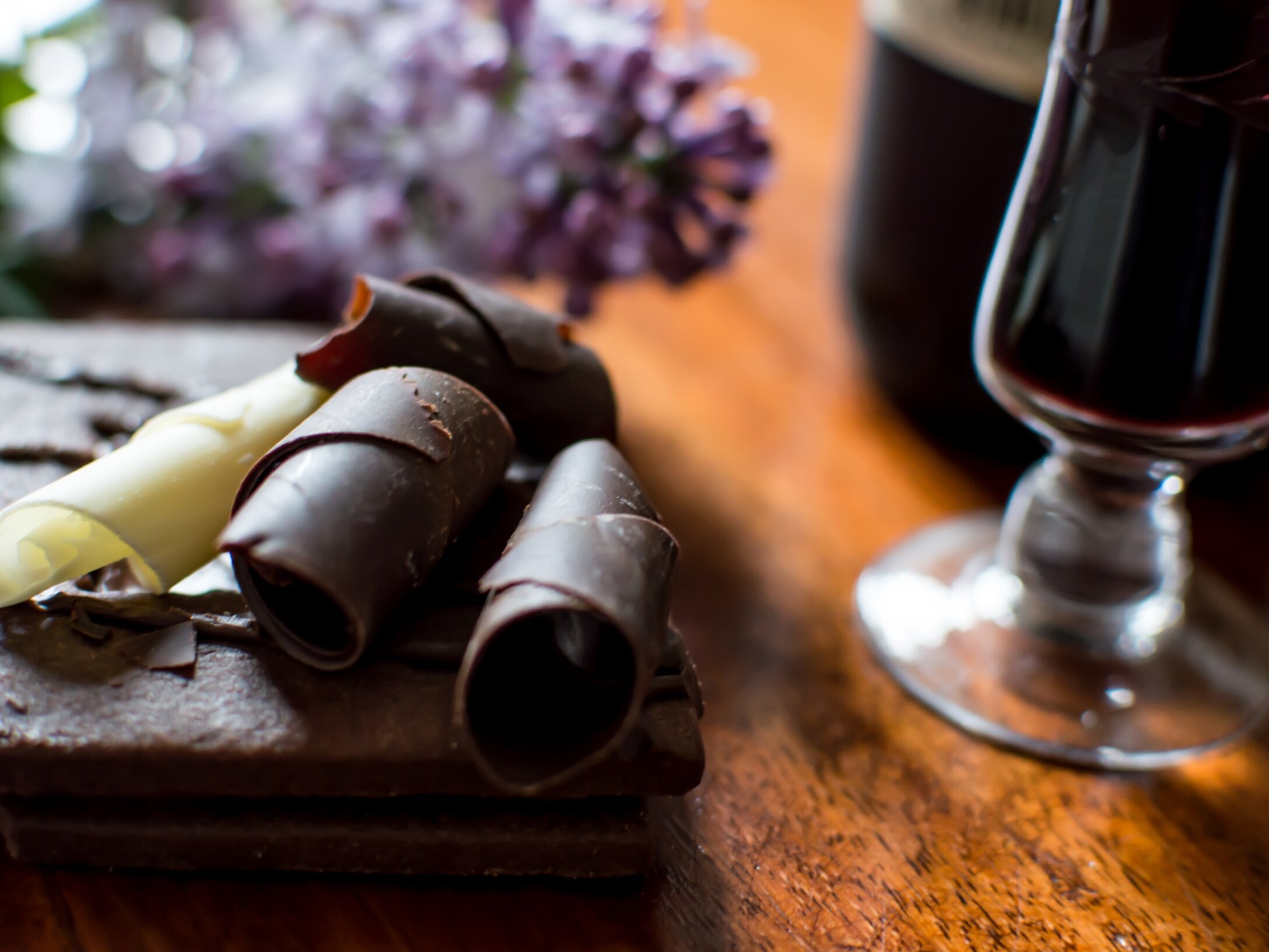 Copa de vino tinto junto a un postre de chocolate con rizos de chocolate amargo y blanco.