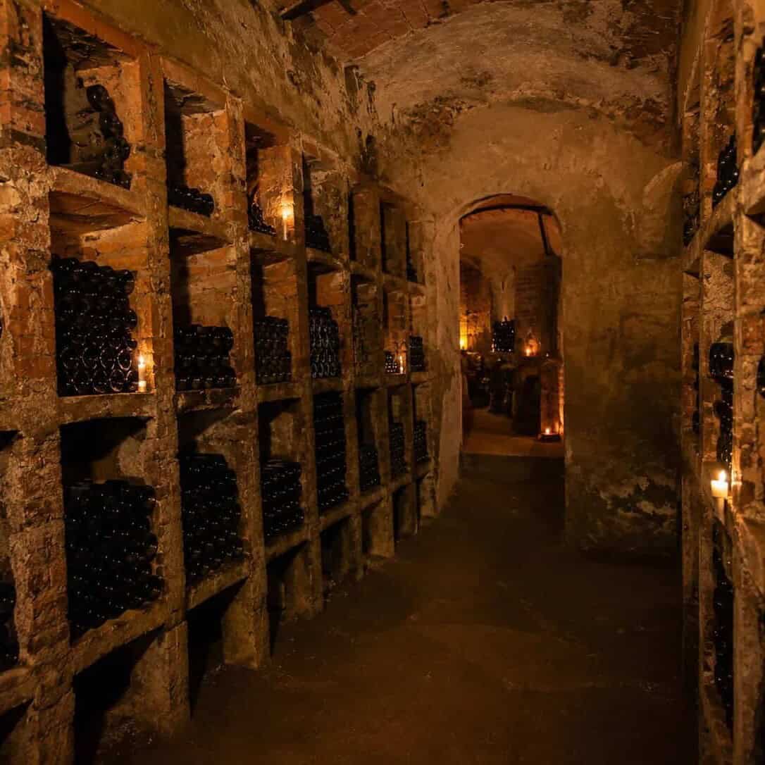Underground wine cellar with bottles, lit by candlelight.