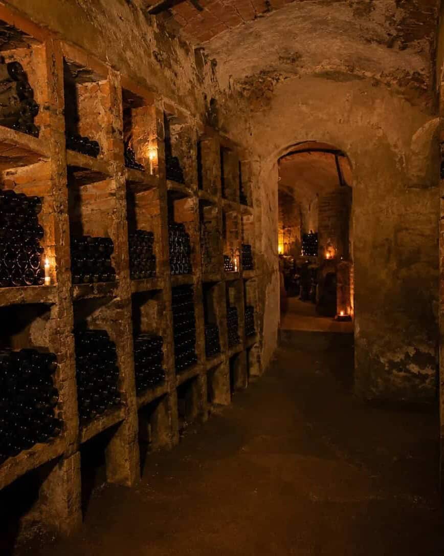 Underground wine cellar with bottles, lit by candlelight.