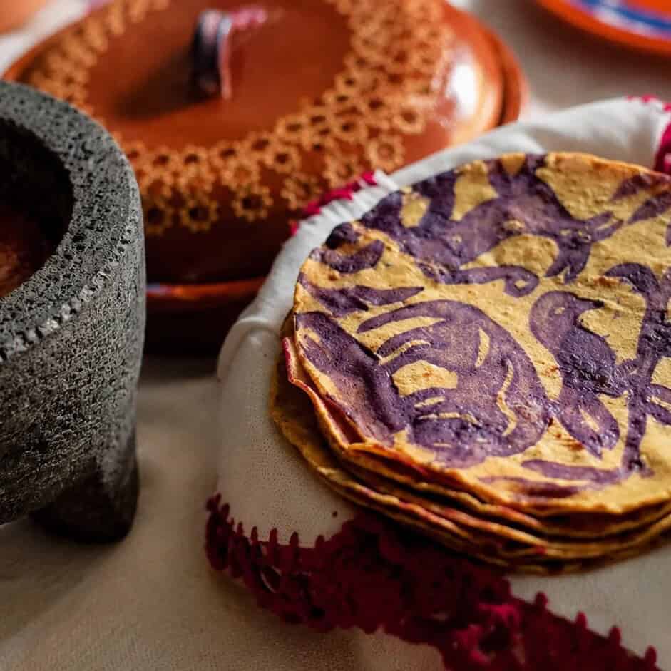 Tortillas de maíz decoradas junto a un molcajete y cazuelas de barro.