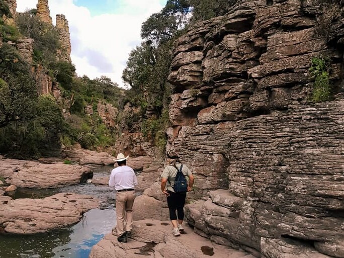 Two hikers walk along a stream between rock walls in Los Panales, Guanajuato.