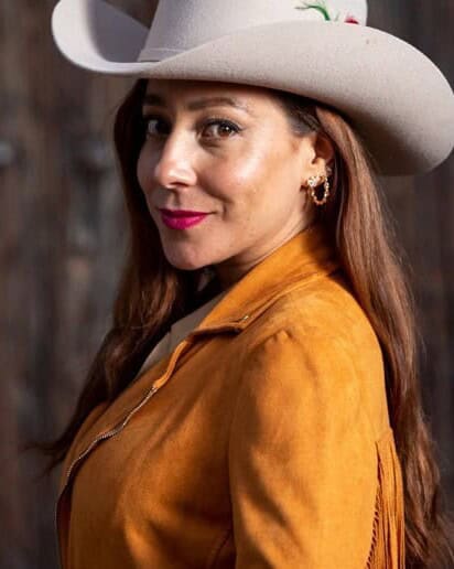 Mujer con sombrero vaquero y chamarra de piel color camel.