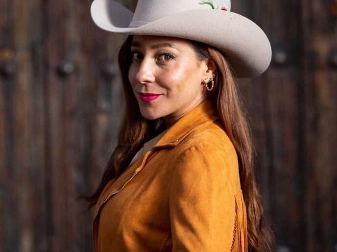 Mujer con sombrero vaquero y chamarra de piel color camel.