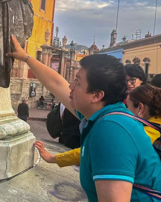 Participantes del tour cultural inclusivo tocan una escultura en el centro histórico de Guanajuato.