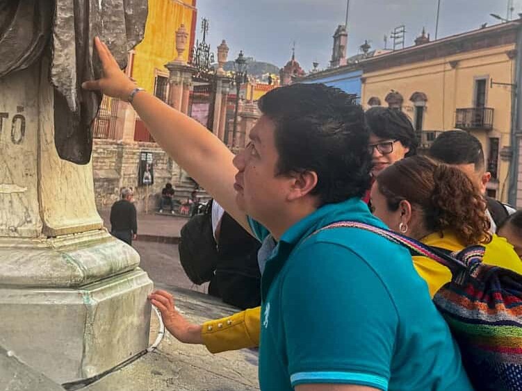 Participantes del tour cultural inclusivo tocan una escultura en el centro histórico de Guanajuato.