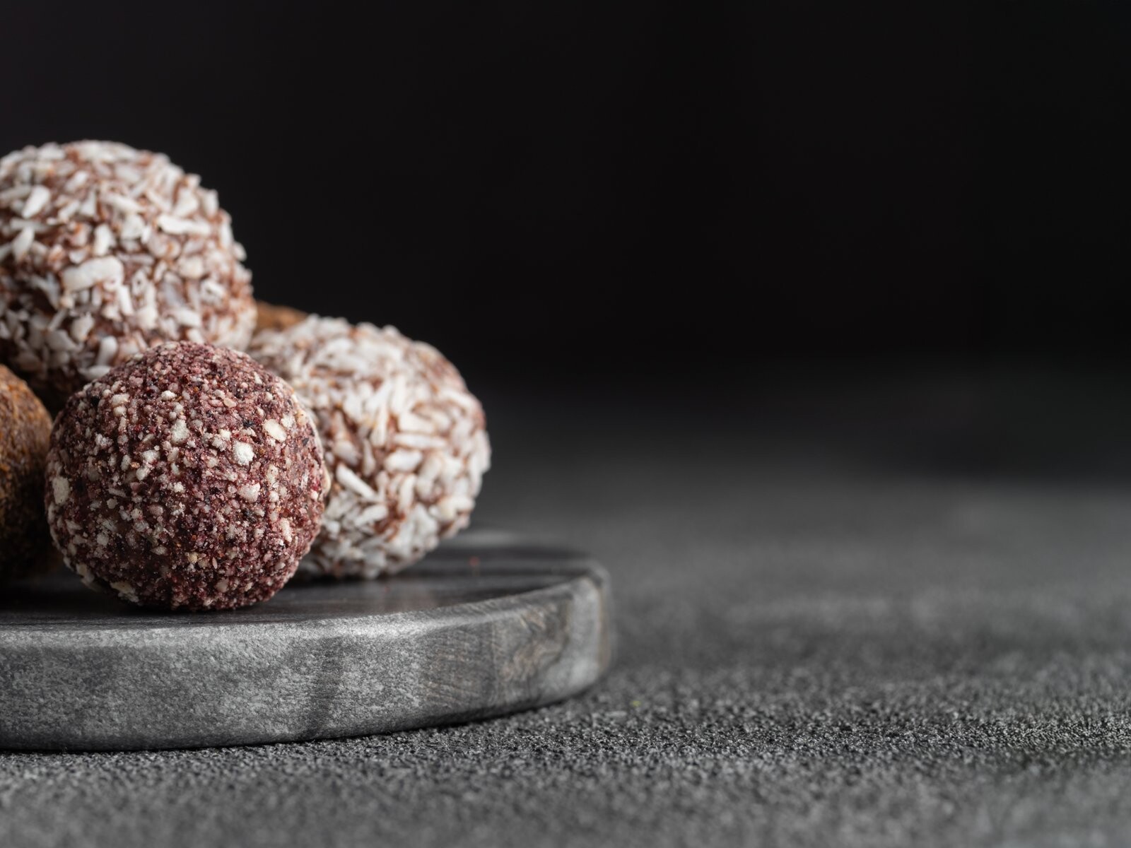 Trufas de chocolate artesanales cubiertas de cacao y coco sobre una base de piedra.