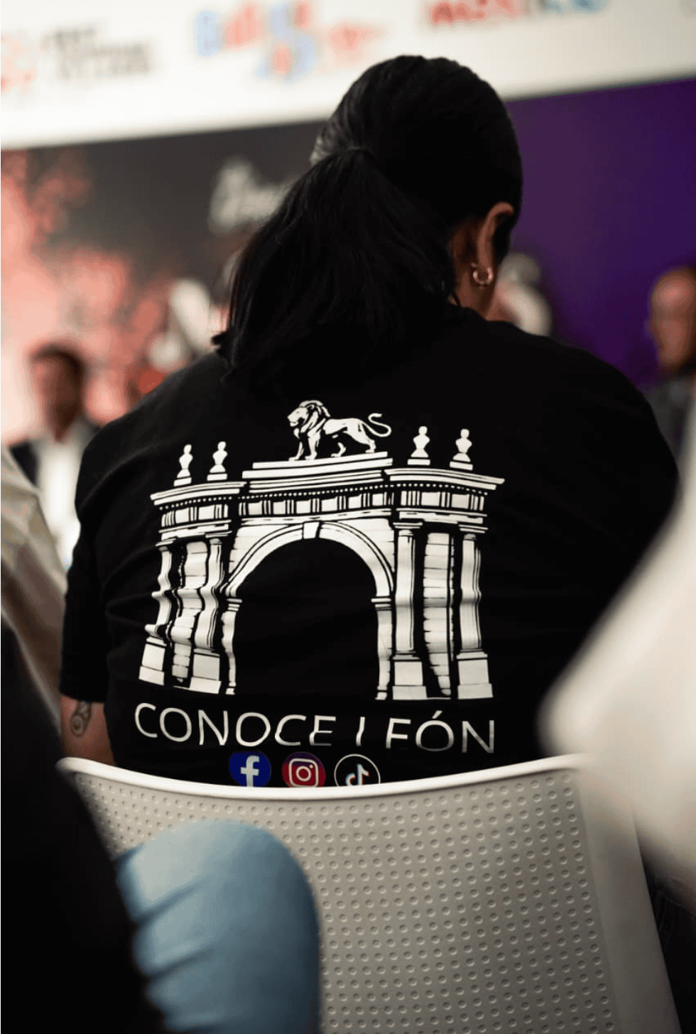 Espalda de una persona con camiseta negra de Conoce Ífón frente a escenario.