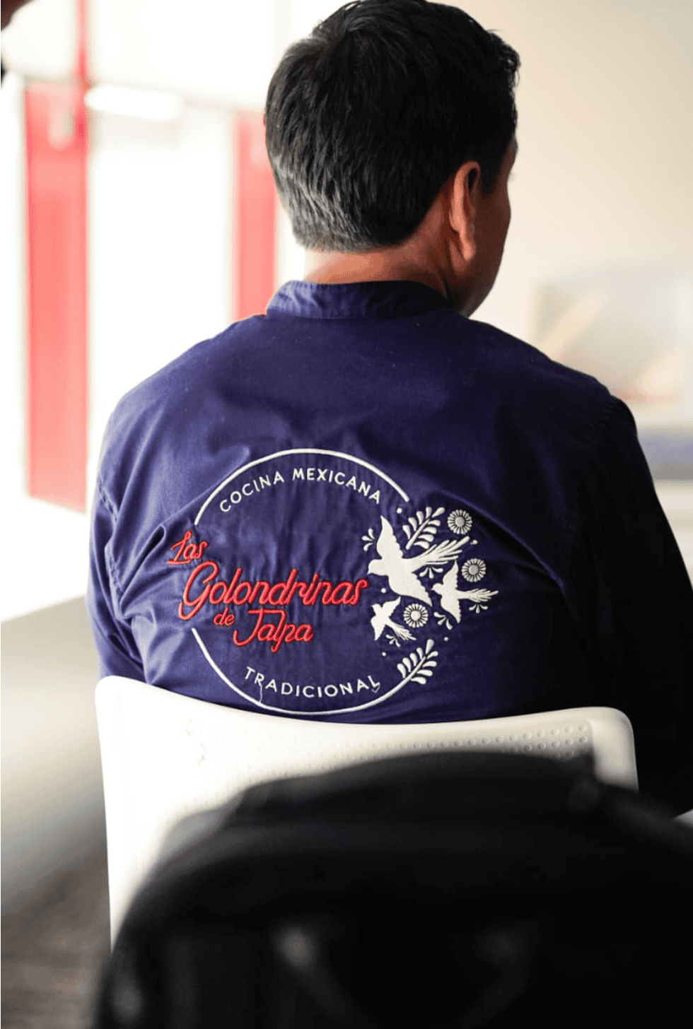 Hombre visto de espalda con chaqueta azul bordada de cocina mexicana tradicional.